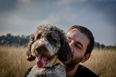 Portrait of man with dog on field against sky