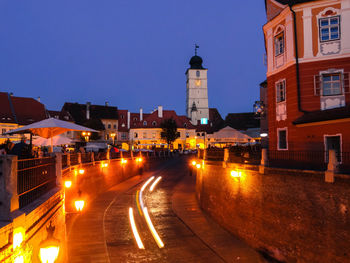 Illuminated street amidst buildings against sky at night