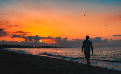 Silhouette man standing on beach against sky during sunset