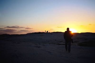 Rear view of silhouette man walking on beach at sunset