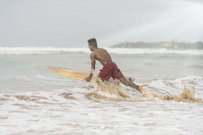 Shirtless man surfing in sea against sky