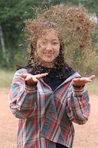 Portrait of smiling teenage girl throwing wood shavings while standing outdoors