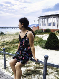 Young woman standing by railing against sky