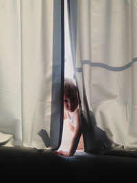 Close-up of boy hiding in curtain at home