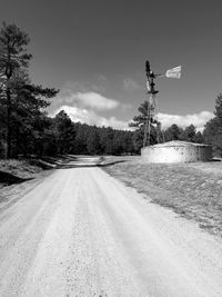 Road by wind turbine and trees against sky