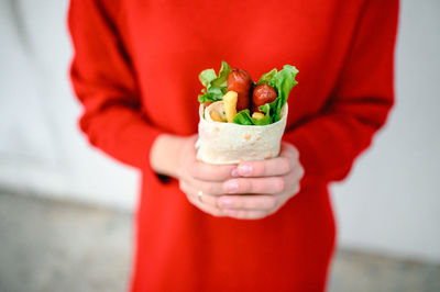 The hands of a girl in red clothes are holding fast street food. shawarma is food in pita