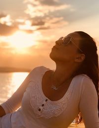 Woman wearing sunglasses against sky at beach during sunset