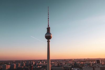 Communications tower in city against sky during sunset