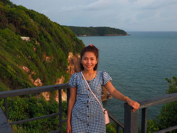 Portrait of smiling woman standing on railing against sea