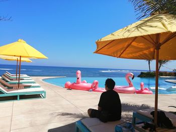 Rear view of people sitting on beach against clear blue sky