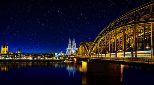 Illuminated bridge over river against sky at night