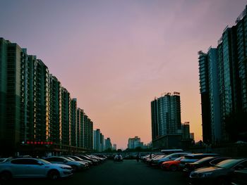 Cars parked on street by buildings against sky during sunset