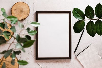  blank frame with white sheet, notepad, pencil and cuts of tree trunk on light background 