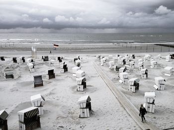 High angle view of hooded beach chairs on sand against cloudy sky