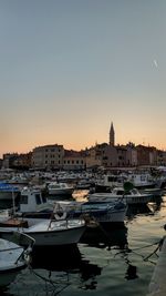 Sailboats moored in harbor against sky during sunset