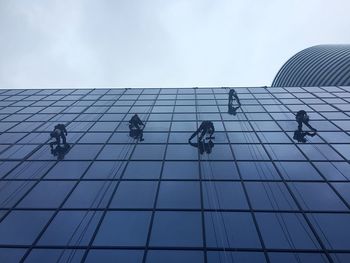 Low angle view of workers cleaning office building against sky
