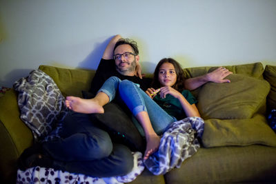 Father and daughter snuggle on couch and watch tv