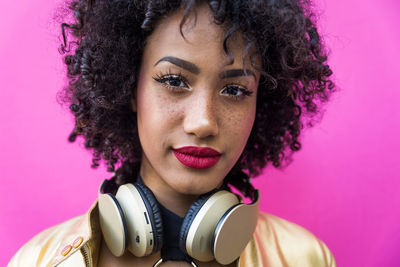 Fashionable young woman with curly hair against pink background