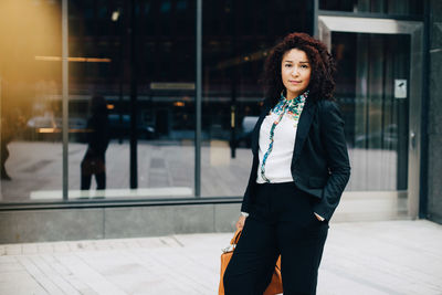 Portrait of confident businesswoman standing against building in city