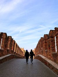 Rear view of people walking on bridge against sky