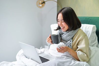 Young woman using phone while sitting on bed at home