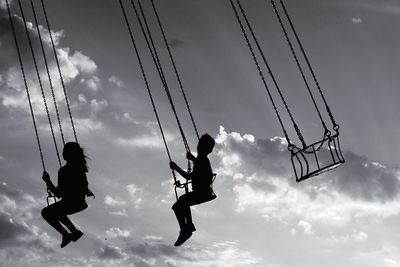 Low angle view of silhouette people enjoying chain swing ride against sky