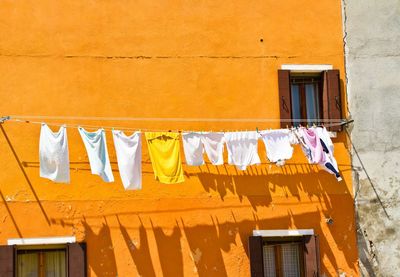 Clothes drying on rope against orange building during sunny day