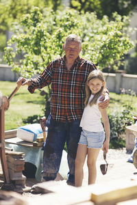 Portrait of grandfather and granddaughter standing by cement mixer in yard