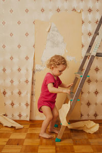 Child tear off the wallpaper from the wall in the room, little mother's helper