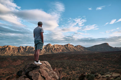 Rear view of man standing on mountain against sky