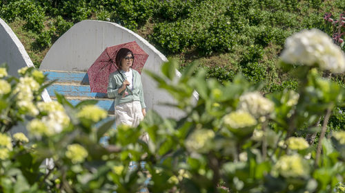 Woman holding umbrella standing by plants