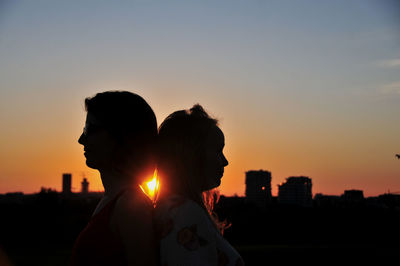 Silhouette people against orange sky in city during sunset