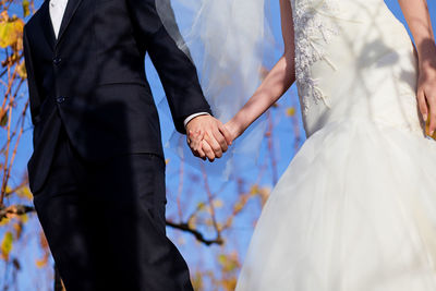 Midsection of bride holding hands of groom while standing outdoors