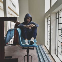 Full length of young man looking away while sitting by window