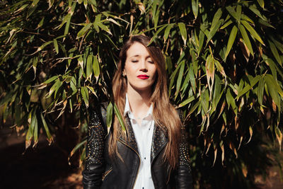 Young woman with eyes closed standing against trees on field in park