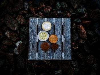 High angle view of coins on wooden plank over stones