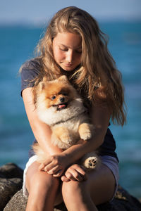 Girl on the sea holding a small dog in her hands