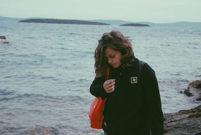 Young woman using phone while standing on beach