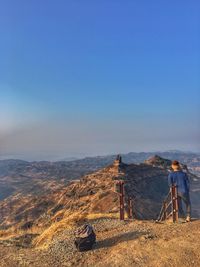 Rear view of man standing on mountain against blue sky