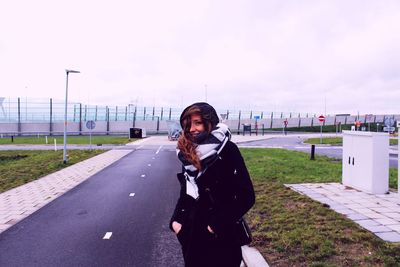 Portrait of smiling young woman wearing warm clothing while standing on road