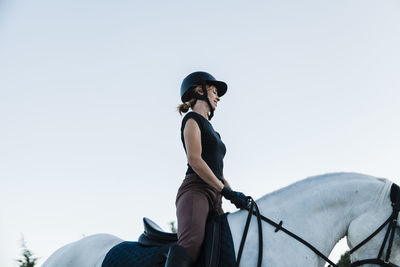 Woman wearing headwear riding horse against clear sky