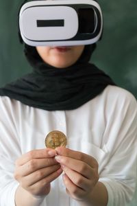 Woman wearing virtual reality simulator while holding bitcoin at home