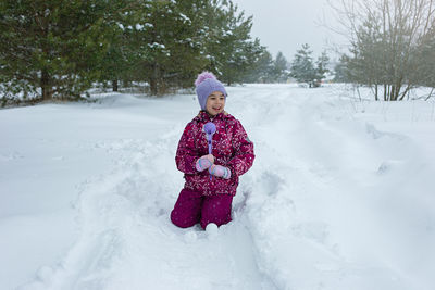 A little girl sits in the snow, makes snowballs using a plastic sculpting tool