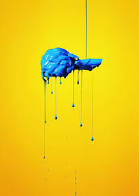 Digital composite of blue paint dripping on artichoke against yellow background