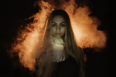 Digital composite image of woman holding candle against black background