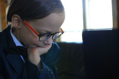 Close-up of boy with hand on chin wearing eyeglasses by brightly lit window