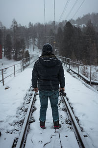 Rear view of young man standing on snow covered railroad track