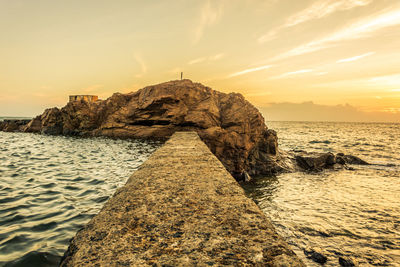 Rock formation on beach against sky during sunset