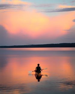 Man rowing boat on lake against sky during sunset