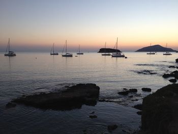 Sailboats in sea at sunset